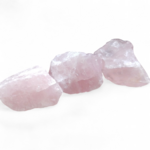 Trois quartz rose bruts rose pâle alignés sur fond blanc lumineux, pierres naturelles reliées à la tendresse, à la sérénité émotionnelle et à l’harmonie intérieure.
