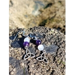Boucles d’oreilles elfiques triquetra en améthyste et sélénite, posées sur rocher côtier face à la mer en Bretagne, pour apaisement et clarté