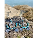 Boucles d’oreilles Atlante en apatite, création Magic Gaïa, sur rocher breton avec mer en arrière-plan, pour calme intérieur et communication posée.