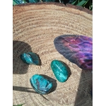 Trois galets de chrysocolle bleu-vert sur tranche de bois avec plume violette en décor, pierres roulées associées à la justesse intérieure, à l’inspiration paisible et à l’harmonie émotionnelle.