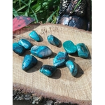 Galets de chrysocolle bleu-vert disposés sur tranche de bois avec végétation en arrière-plan, pierres roulées évoquant la confiance tranquille, la respiration émotionnelle et l’harmonie.