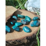 Galets de chrysocolle bleu-vert posés sur tranche de bois avec plantes vertes en lumière naturelle, pierres roulées associées à la douceur, au calme du cœur et à l’équilibre intérieur.