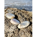 Trois galets de pierre de lune aux reflets nacrés posés sur un rocher face à la mer en Bretagne, pierres naturelles évoquant la fluidité intérieure, la rêverie et la tranquillité.
