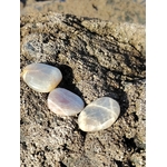 Trois galets de pierre de lune aux reflets nacrés posés sur un rocher texturé en lumière naturelle, pierres naturelles associées à la sérénité, à la présence à soi et à la douceur émotionnelle.