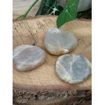 Trois galets de pierre de lune gris nacré posés sur une tranche de bois avec une feuille verte, décor naturel, pierres naturelles liées à la tendresse, au recentrage et à l’équilibre du cœur.
