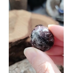 Pierre roulée de grenat almandin rouge sombre tenue entre deux doigts, surface polie aux reflets profonds, pierre naturelle associée à l’assurance, à la solidité et à l’élan vital.