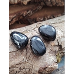 Trois pierres roulées d’hyperstène noir aux reflets métalliques posées sur du bois naturel, éclats subtils, pour inviter à l’ancrage, la protection et la clarté mentale.