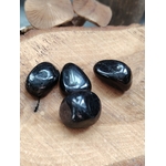 Quatre pierres roulées d’hyperstène noir brillant posées sur une tranche de bois, reflets profonds, pour inviter à l’ancrage, la protection et la clarté mentale.