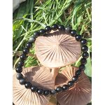 Bracelet obsidienne œil céleste 6 mm sur rondins en bois au milieu d’herbes vertes, perles noires, force calme, vigilance et enracinement