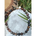 Bracelet en piétersite 6 mm aux perles bleu-brun posé sur une géode blanche, écorce et brins d’herbe en décor; ancrage, clarté mentale, confiance.