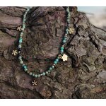 Gros plan sur collier doré en acier inoxydable avec perles facettées vert africain et pendentifs fleur, éclat lumineux sur rochers bruns