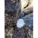 Bague réglable en argent 925 sertie d’une péristérite (pierre de lune arc-en-ciel) ovale, posée sur roche sombre en bord de mer, reflets bleutés, intention douceur et intuition.