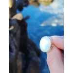 Bague réglable en argent 925 sertie d’une péristérite ovale (pierre de lune arc-en-ciel), tenue entre les doigts face à la mer de Bretagne, reflets bleutés, intention apaisement et intuition.