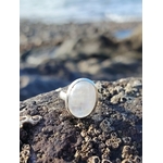 Bague réglable en argent 925 sertie d’une péristérite ovale (pierre de lune arc-en-ciel) posée sur roche granitée en bord de mer, reflets laiteux, intention apaisement et intuition.