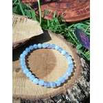 Bracelet calcédoine bleue 6 mm sur coupe de bois brut au soleil, herbe haute, disque gravé et plume violette, douceur relationnelle et expression sereine.