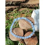 Bracelet calcédoine bleue 6 mm posé sur champignons en bois dans l’herbe avec écorce et géode de quartz, écoute paisible et stabilité affective