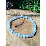 Bracelet calcédoine bleue 6 mm sur tranche de bois clair veinée avec herbe floue, parole douce, calme du cœur et fluidité émotionnelle.