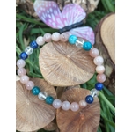 Bracelet bien-être en pierres naturelles photographié de biais sur bois brut, nuances pêche, bleu nuit et transparent pour assurance intérieure et rayonnement doux