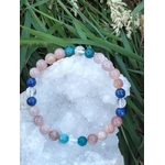 Bracelet bien-être 6 mm posé sur géode de quartz blanc dans l’herbe, lapis-lazuli, pierre de soleil, apatite et cristal de roche pour clarté mentale et parole apaisée