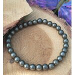 Bracelet pyrite 6 mm gris anthracite métallisé en perles rondes posé sur un rondin de bois, avec aile violette en décor, évoquant la maîtrise de soi, l’élan protecteur et la solidité intérieure