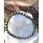Bracelet pyrite 6 mm gris anthracite métallisé en perles rondes présenté sur un amas de quartz c, dans un décor minéral naturel, évoquant la solidité, la vigilance et la force intérieure