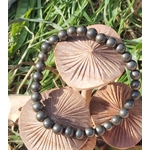 Bracelet pyrite 6 mm en perles rondes présenté sur des champignons décoratifs au milieu de l’herbe, évoquant la force mentale, la détermination et l’assurance intérieure