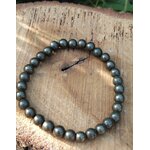 Bracelet pyrite 6 mm gris anthracite métallisé en perles rondes posé sur un support en bois, sous lumière naturelle, évoquant la concentration, la ténacité et l’ancrage mental