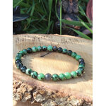 Bracelet rubis zoïsite 6 mm sur tranche de bois avec écorce, herbe floutée et petites statuettes, ancrage stable, courage tranquille et confiance en soi