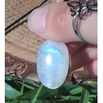 Pendentif labradorite blanche ovale en argent 925, tenu entre les doigts au soleil, fond bois et herbe, pierre naturelle évoquant le recentrage, l’apaisement et la sensibilité intuitive.