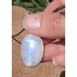 Pendentif ovale en labradorite blanche argent 925, tenu entre les doigts au soleil avec reflet bleu, cordon noir visible, bijou en pierre naturelle associé à la délicatesse, au calme et à l’inspiration intérieure.