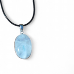Pendentif ovale en labradorite blanche sertie argent 925 sur cordon noir, posé sur pierre beige au soleil, bijou en pierre naturelle relié à la clarté, à la sérénité et à la perception fine.
