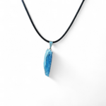 Pendentif en cyanite bleue brute sur cordon noir, suspendu sur fond clair épuré, création Magic Gaïa; intention: apaisement, clarté mentale et communication douce.