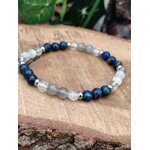Bracelet migraine 6 mm en lapis lazuli, labradorite et sélénite présenté sur un rondin de bois, avec feuillage sombre en arrière-plan, pour clarté, apaisement et détente.