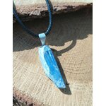 Pendentif en cyanite bleue brute sur cordon noir, bélière argentée, posé sur rondin de bois au soleil; intention: clarté, apaisement.