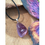 Pendentif en amétrine aux reflets violets sur cordon noir, posé sur bois avec décor minéral coloré, pierre naturelle associée à la clarté, à l’inspiration et à l’équilibre intérieur.