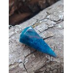 Pendule en apatite bleue facettée posé sur une écorce naturelle aux reliefs marqués, dans une ambiance brute et minérale, évoquant intuition, apaisement émotionnel et clarté intérieure.