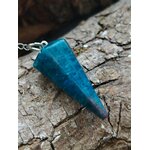 Pendule en apatite bleue facettée posé sur une écorce naturelle aux tons bruns, dans une ambiance minérale et boisée, évoquant intuition, apaisement émotionnel et clarté intérieure.