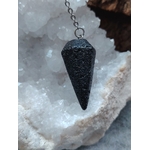 Pendule en pierre de lave noire présenté sur un amas de quartz blanc dans un décor minéral naturel, une mise en scène évoquant ancrage, stabilité et recentrage.