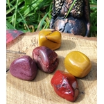 Pierres roulées de jaspe mookaïte posées sur support en bois avec herbes en lumière naturelle, pierres naturelles associées à l’ancrage, à la stabilité intérieure et à l’énergie chaleureuse.