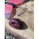 Pierre roulée de jaspe mookaïte bordeaux posée sur un support en bois près d’un lien noir et d’un décor coloré, pierre naturelle liée à la maîtrise de soi, à l’endurance et à l’ancrage.