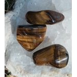 Trois pierres roulées œil de tigre aux reflets bruns et dorés posées sur un amas de quartz, pierres naturelles évoquant la force tranquille, la solidité émotionnelle et la vigilance intérieure.