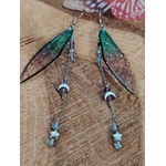 Boucles d’oreilles fée création Magic Gaïa posées sur bois brut, avec ailes translucides bleu-vert, pampilles argentées, lunes et étoiles, dans une ambiance féerique, douce et inspirante au quotidien.