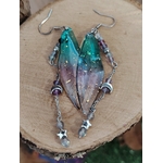 Boucles d’oreilles fée création Magic Gaïa posées sur une tranche de bois, avec ailes translucides bleu-vert, fines pampilles argentées, lunes et étoiles, dans une ambiance féerique inspirant douceur et légèreté.