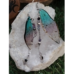 Boucles d’oreilles fée création Magic Gaïa posées sur un amas de quartz, avec ailes translucides bleu-vert, chaînettes fines et perles sombres, pour une ambiance poétique, apaisante et féerique