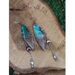 Boucles d’oreilles fée création Magic Gaïa posées sur bois naturel, avec ailes translucides bleu-vert et pampilles fines, dans une ambiance féerique, douce et inspirante favorisant l’évasion et la légèreté.