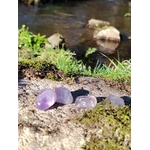 Pierres roulées d’améthyste posées sur un rocher moussu, entourées d’herbes et de lumière naturelle, dans une ambiance sereine évoquant intuition, apaisement et équilibre intérieur.