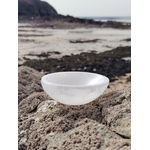 Bol chantant en sélénite 10 cm posé sur rocher granitique face à la mer en Bretagne, vagues et îlot au loin, pour une atmosphère sereine favorisant apaisement et clarté.