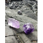 Deux améthystes brutes violettes posées sur rochers bretons près de l’eau, textures minérales et reflets marins, pour une énergie douce d’apaisement et de clarté.