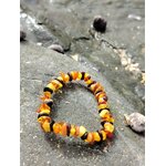 Bracelet enfant ambre baroque formé en cercle sur rocher breton, nuances miel et cognac, apaisement tendre et ambiance lumineuse