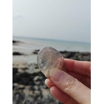 Galet en quartz rose bleu naturel tenu à la main face à la mer en Bretagne, pierre naturelle évoquant le réconfort, l’écoute de soi et la tranquillité émotionnelle.